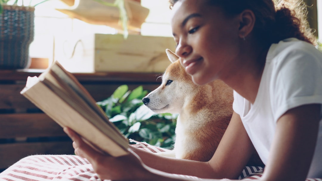 who-we-are Close-up shot of African American girl dog owner reading book lying on bed in modern flat near adorable obedient pet. Interesting hobby, literature and domestic animals concept.